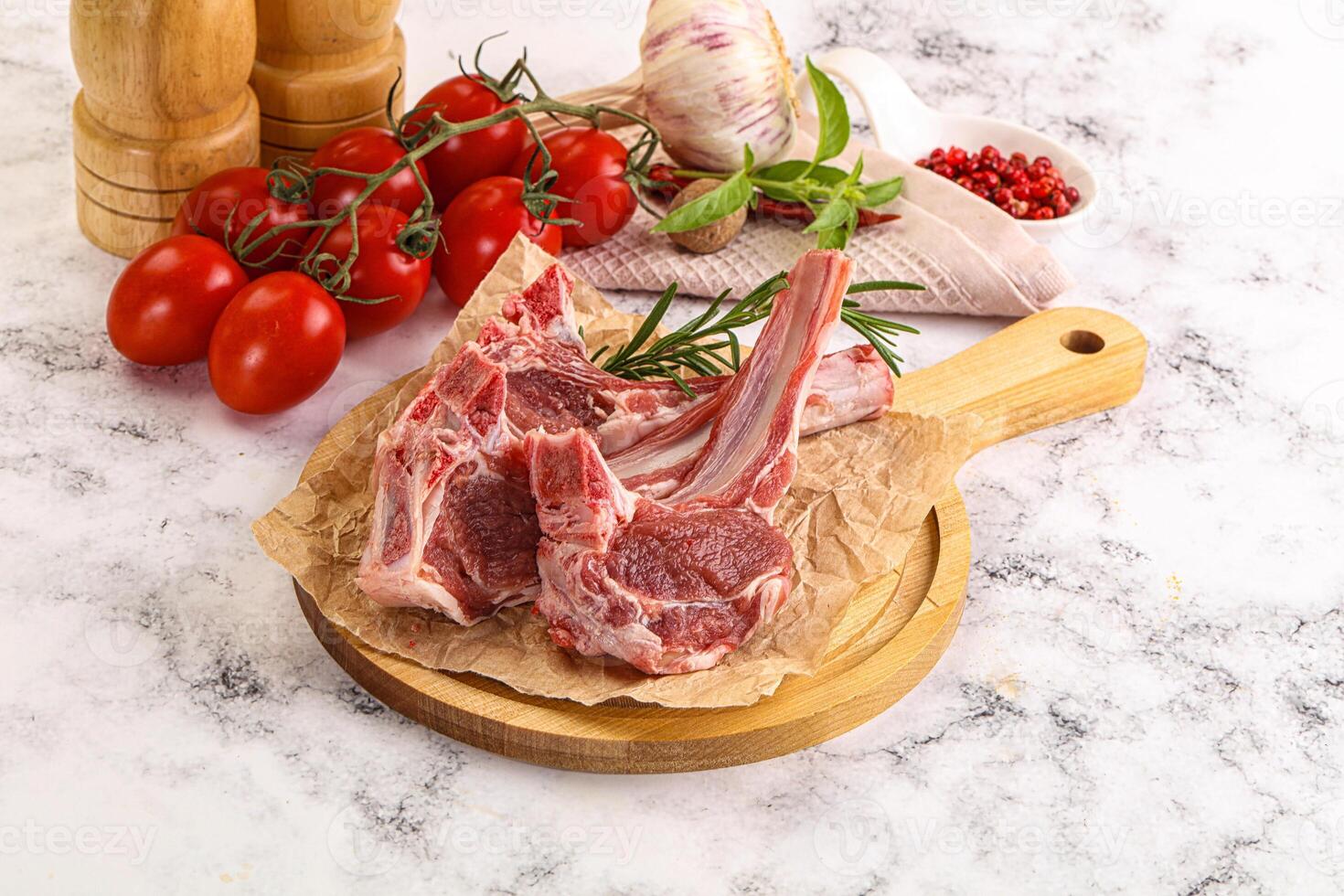 A cutting board with two lamb chops and a tomato photo