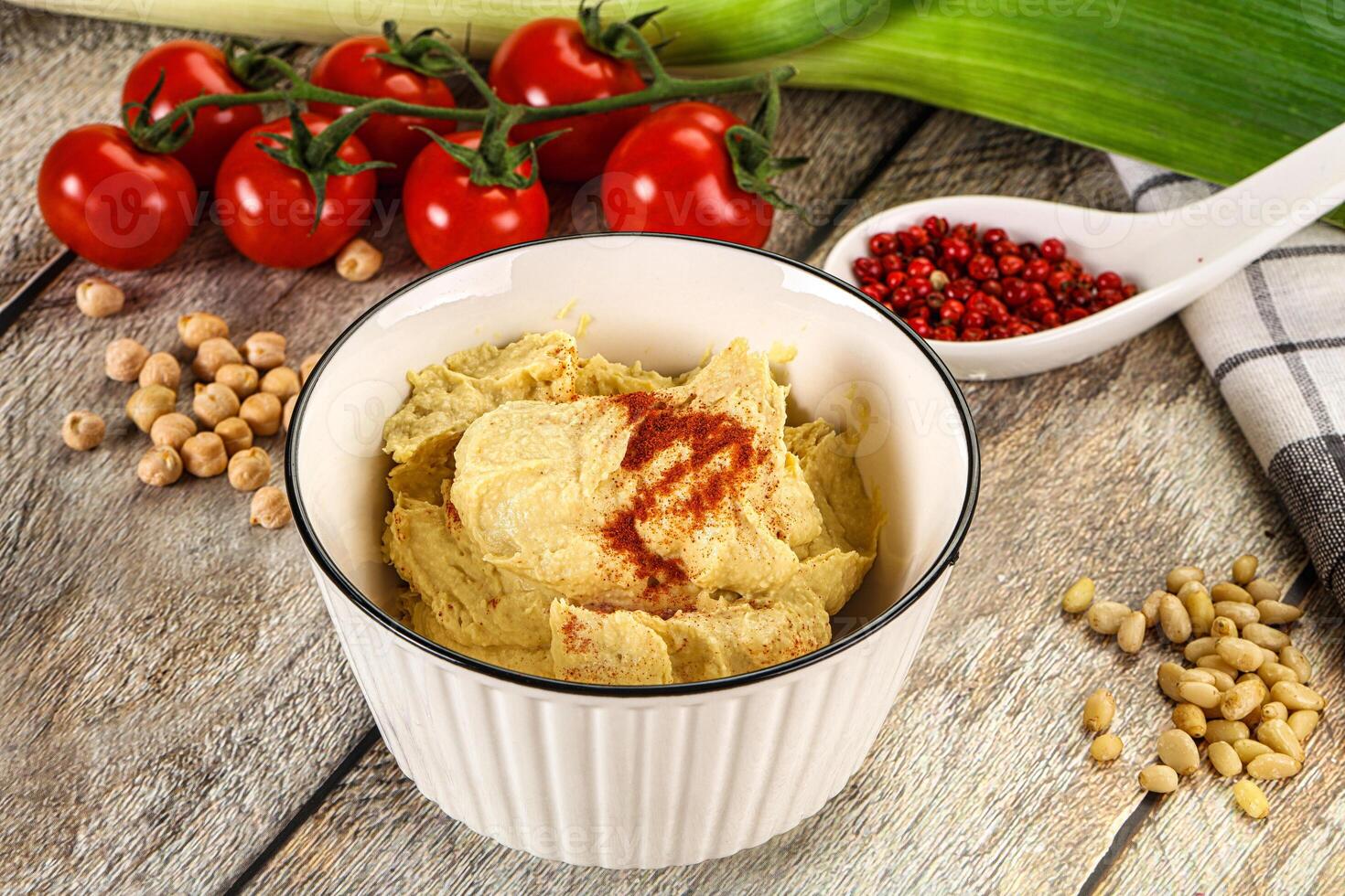 A bowl of hummus with a spoon and tomatoes photo
