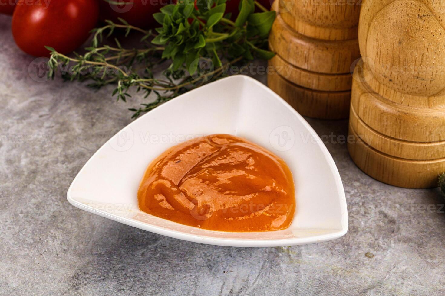 A bowl of tomato sauce next to a pepper and a wooden spoon photo