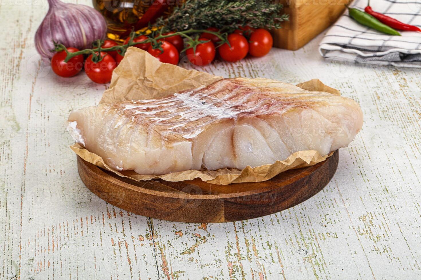 A piece of fish on a wooden plate with tomatoes and herbs photo