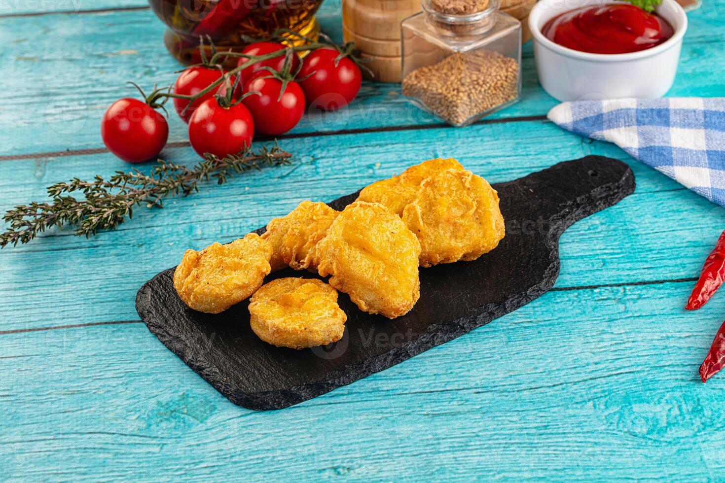Fried chicken nuggets on a black board with spices and tomatoes photo