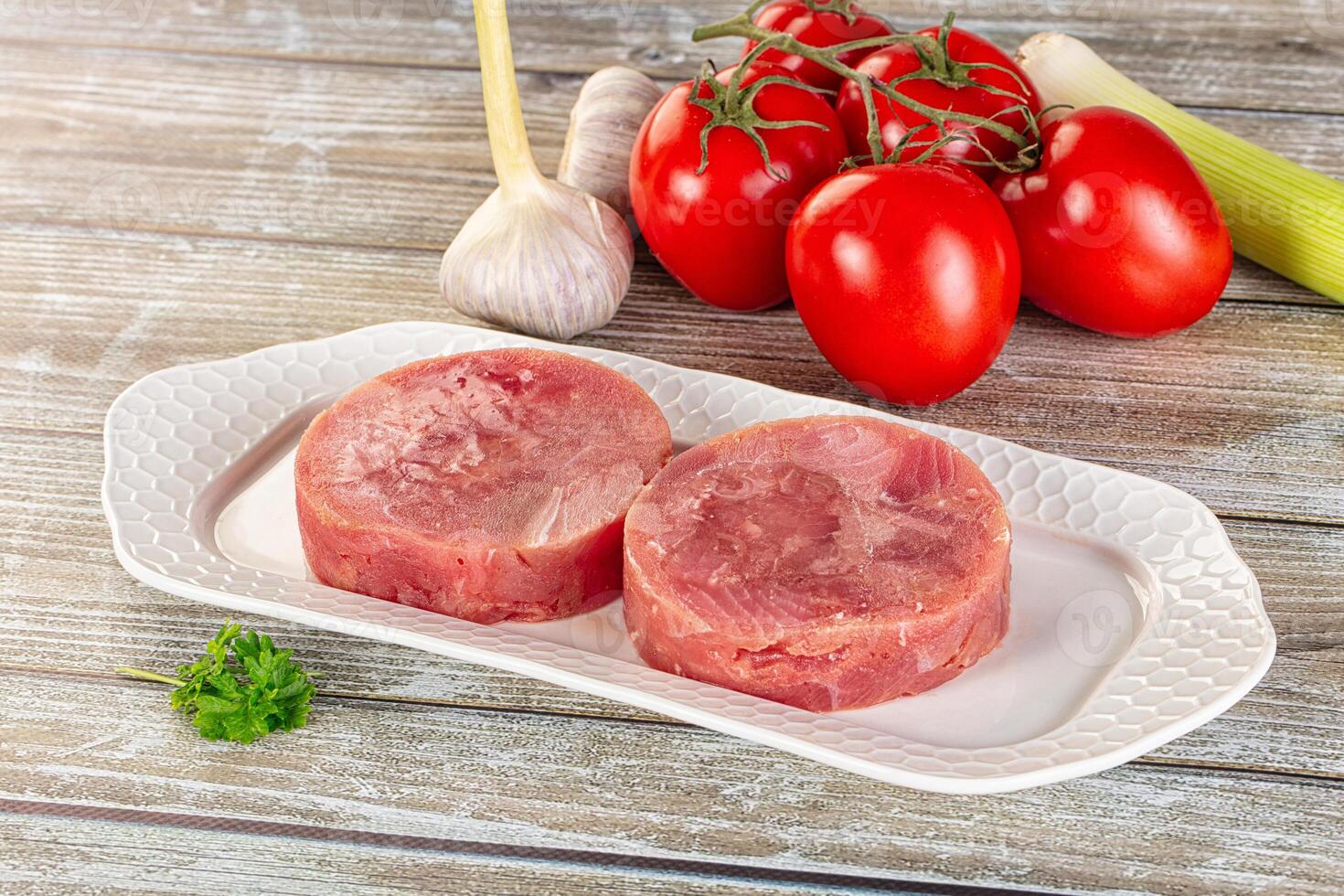 Two raw meat patties on a white plate with tomatoes and herbs photo