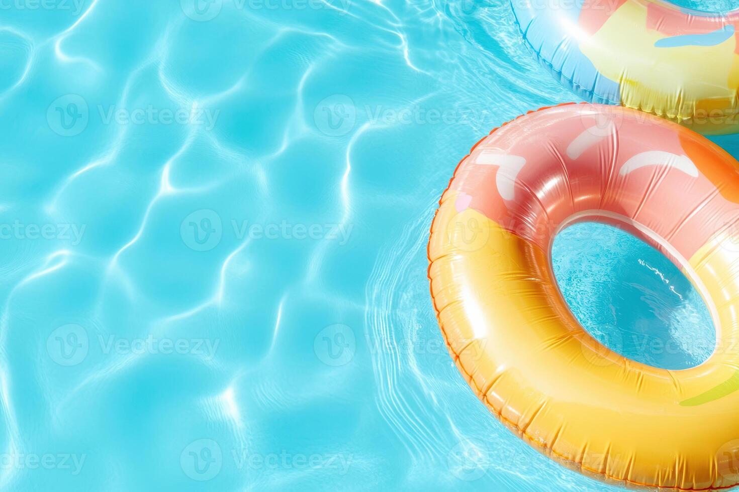 Bright inflatable pool rings floating in clear blue water under sunlight photo