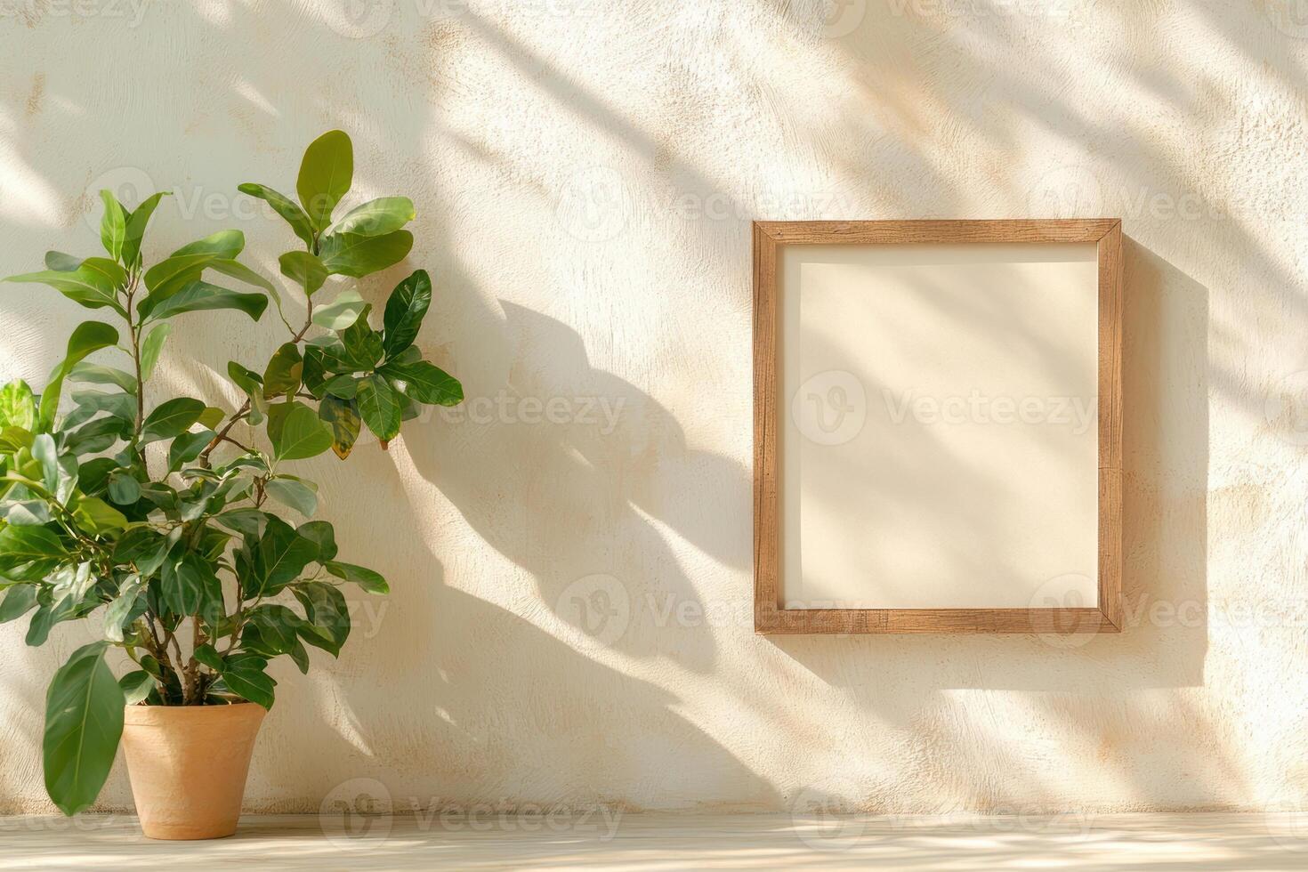 Framed empty canvas on sunlit wall beside green indoor plant in terracotta pot casting natural shadows photo