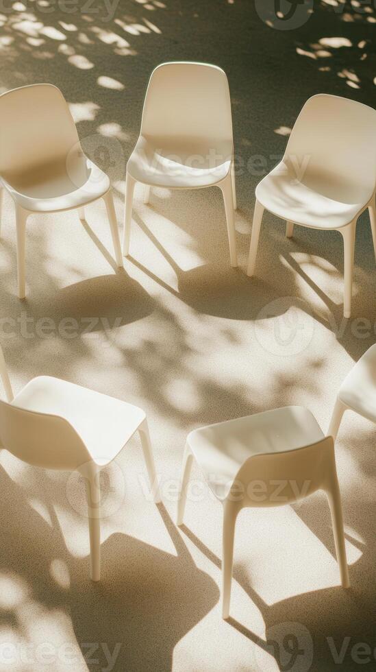 Sunlit circle of white chairs on textured floor under dappled tree shadows, creating a peaceful outdoor setting photo