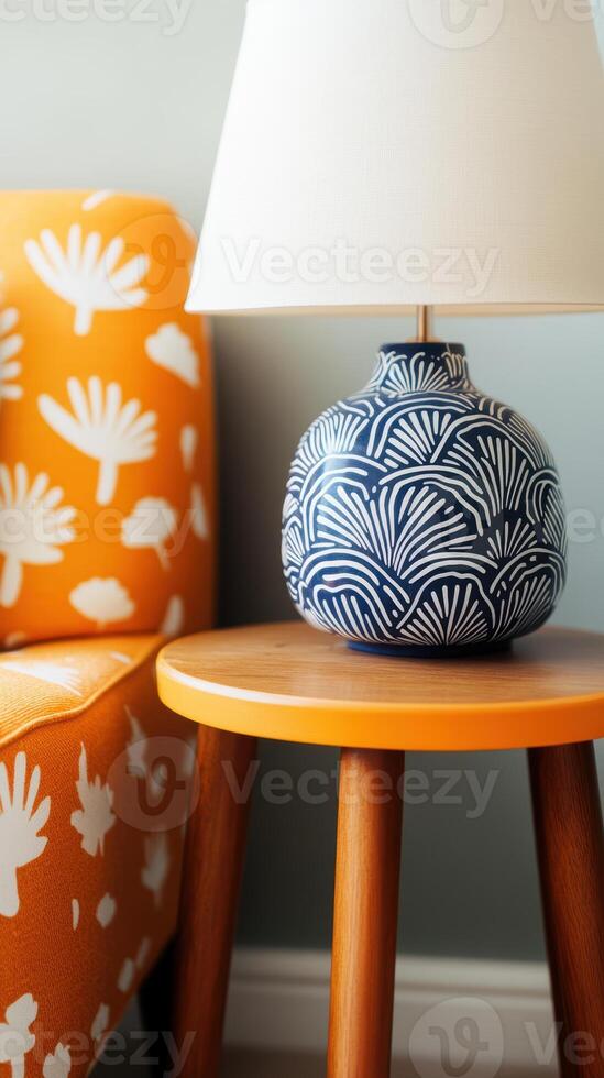 Blue and white patterned lamp on wooden table beside bright orange floral armchair photo
