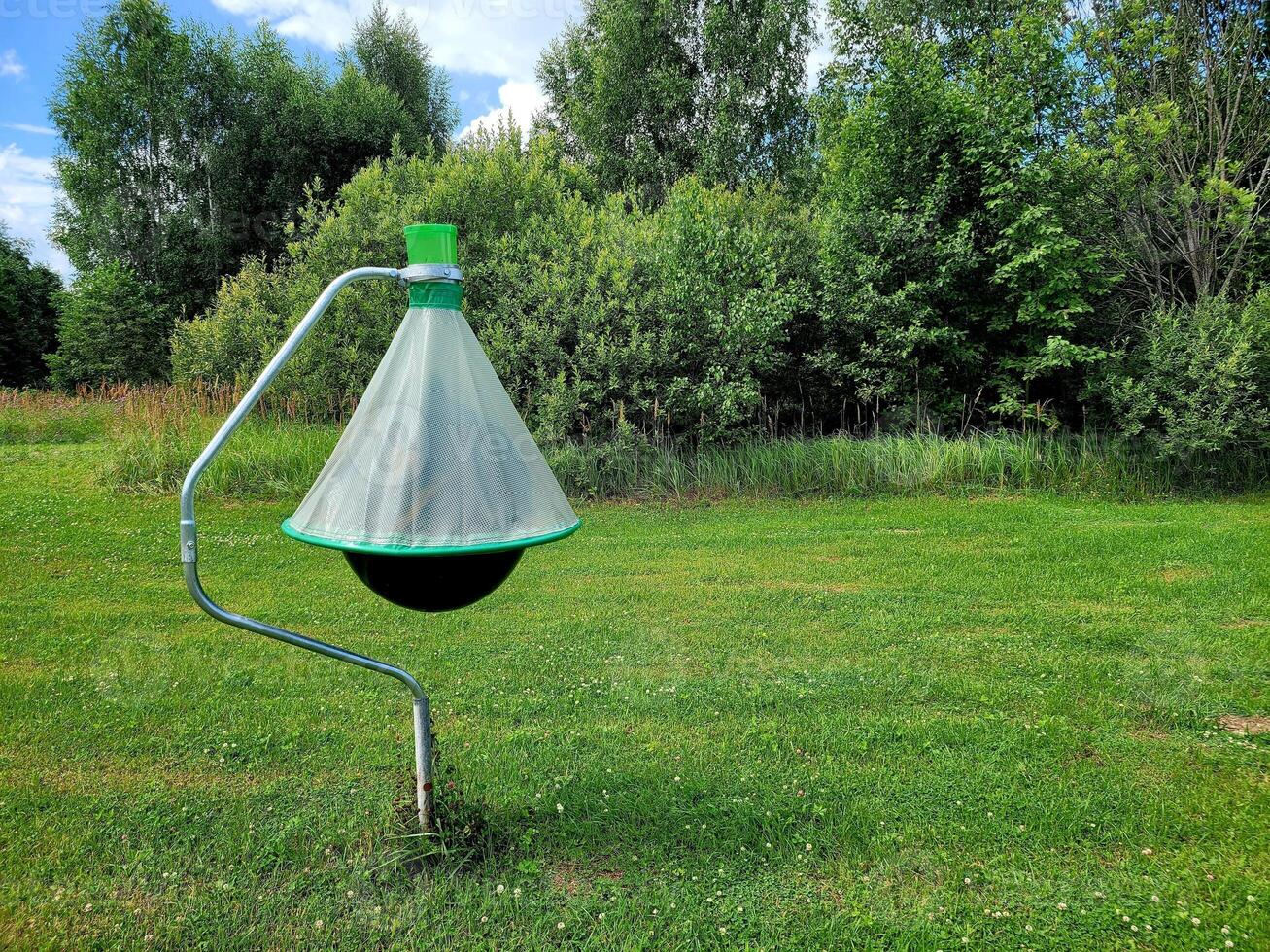Horsefly trap against green trees. Photo black ball insect trap on stand in mown meadow. Agricultural equipment for insect protection.