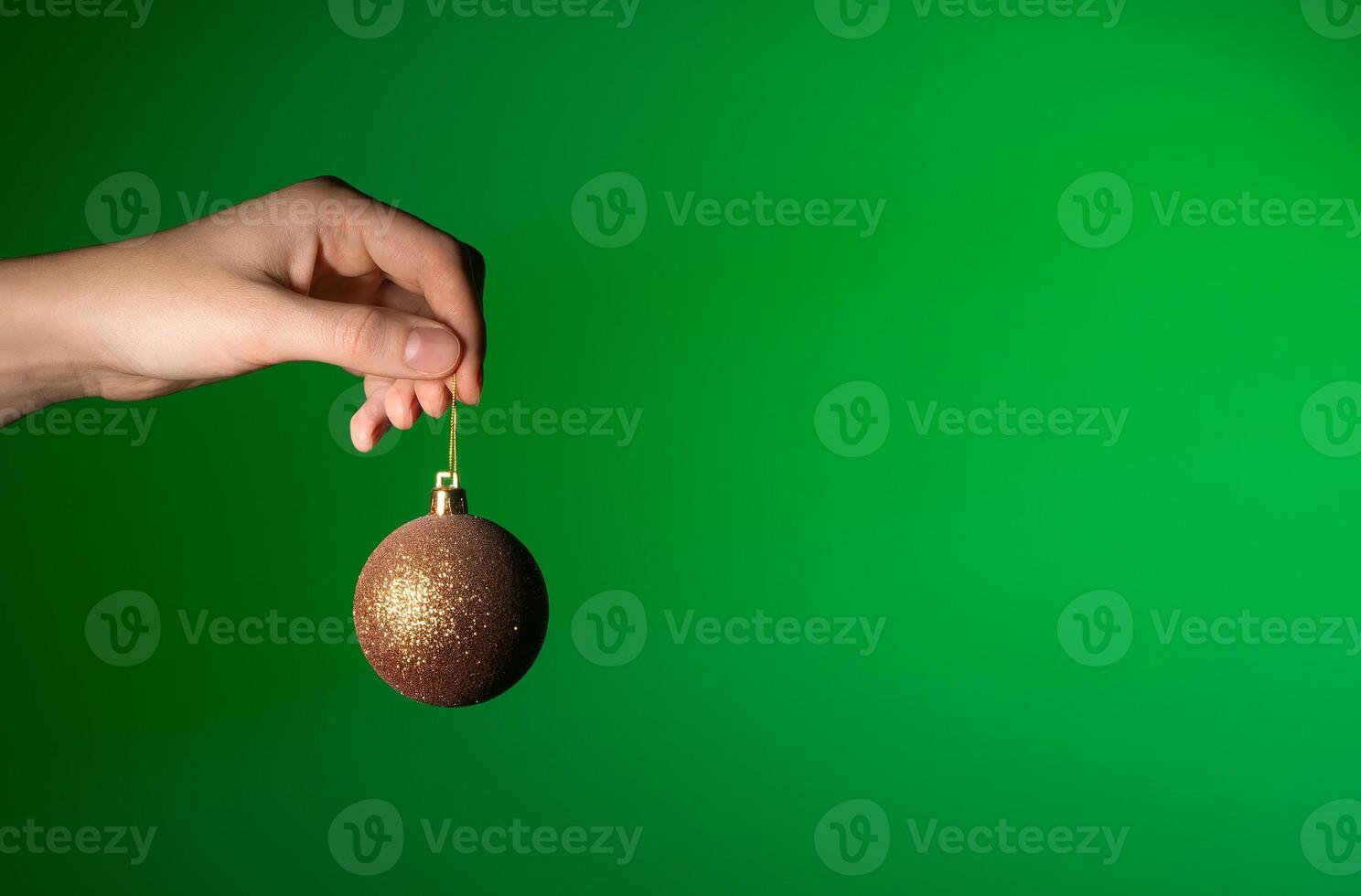 Christmas bauble in hand, festive golden ornament for holiday decoration. Round glass sphere hanging photo