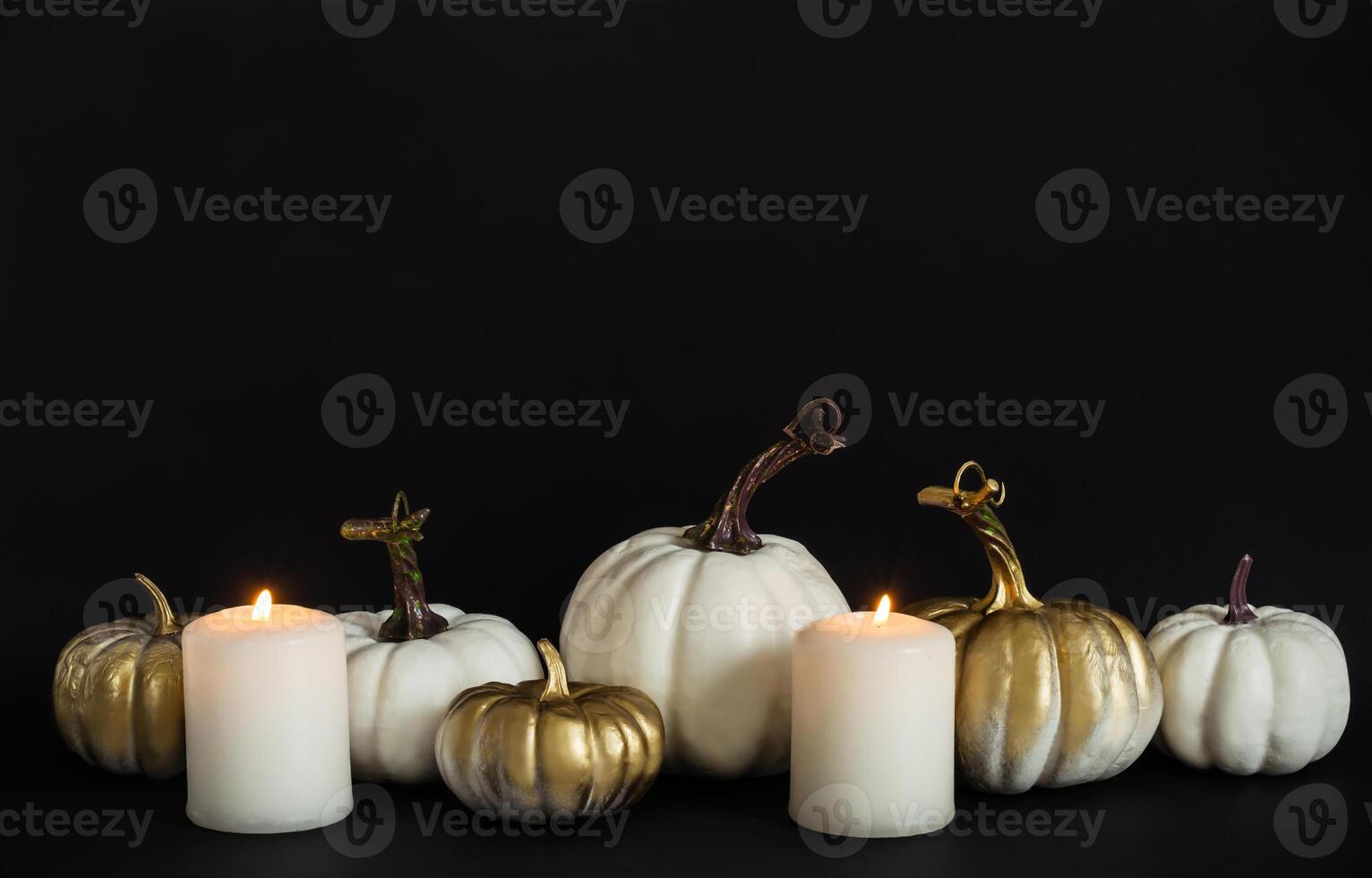 White, golden pumpkins and burning candles on black background. Halloween concept photo