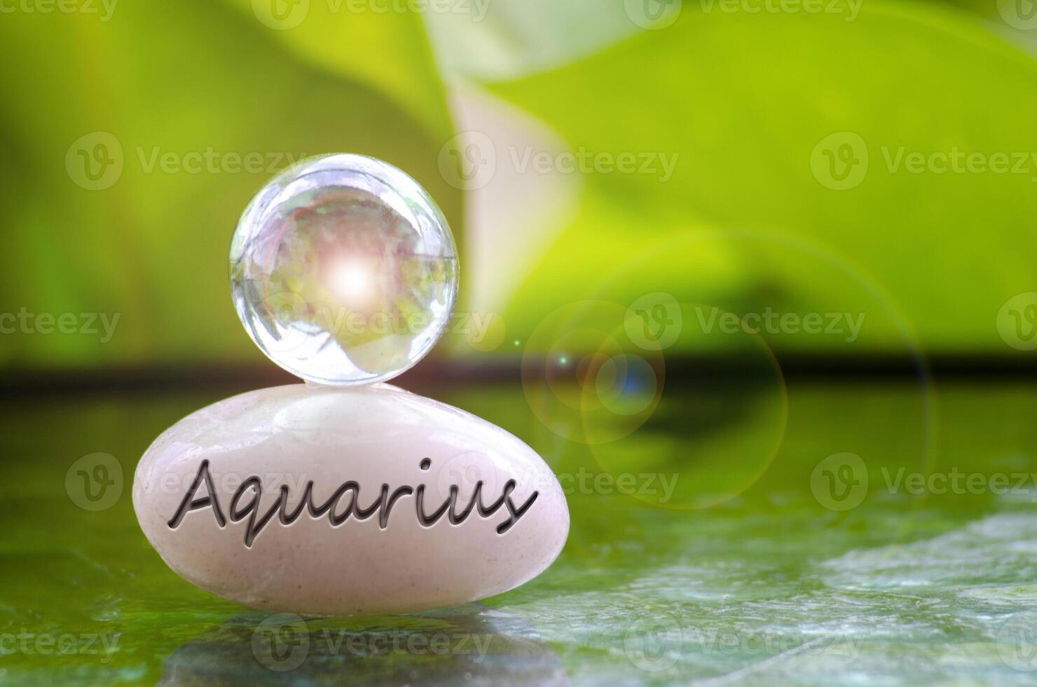 Aquarius text engraved on Zen stone with shining glass marble on top. Zodiac concept photo
