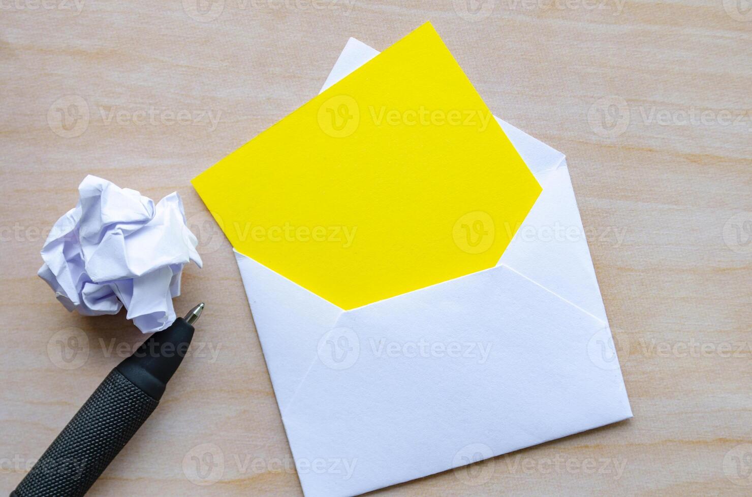 Top view of empty yellow notepad inside an envelope with crumpled paper and pen with customizable space for text photo