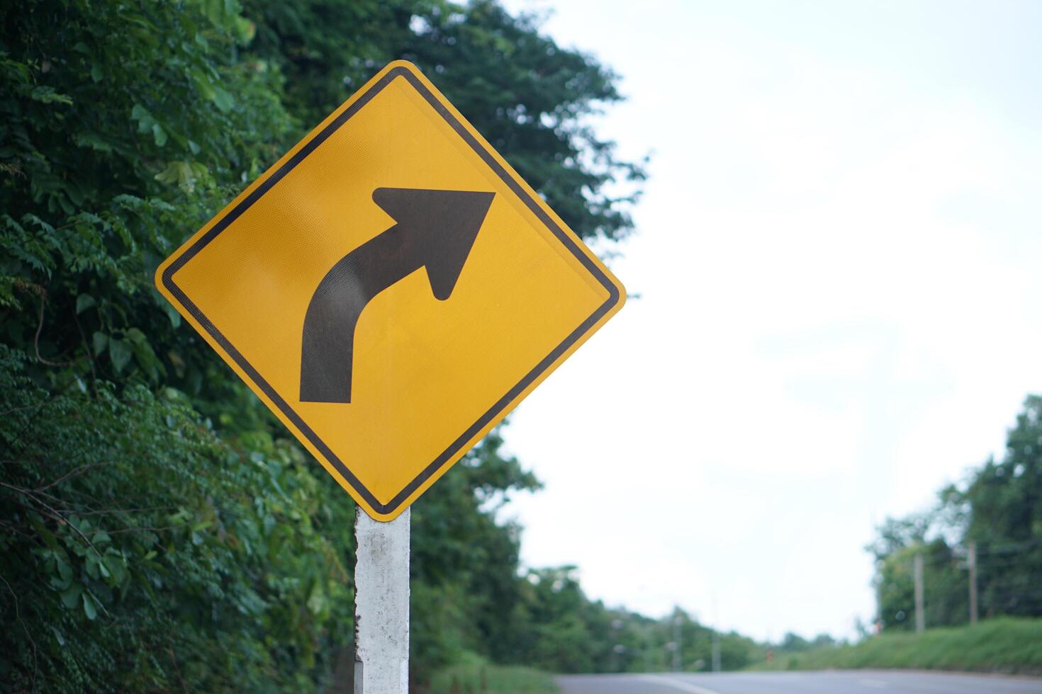 Yellow traffic sign with arrow right curve symbol beside the rural road to warn drivers to know the way ahead has right curve. Concept. Warning traffic sign for transportation. photo