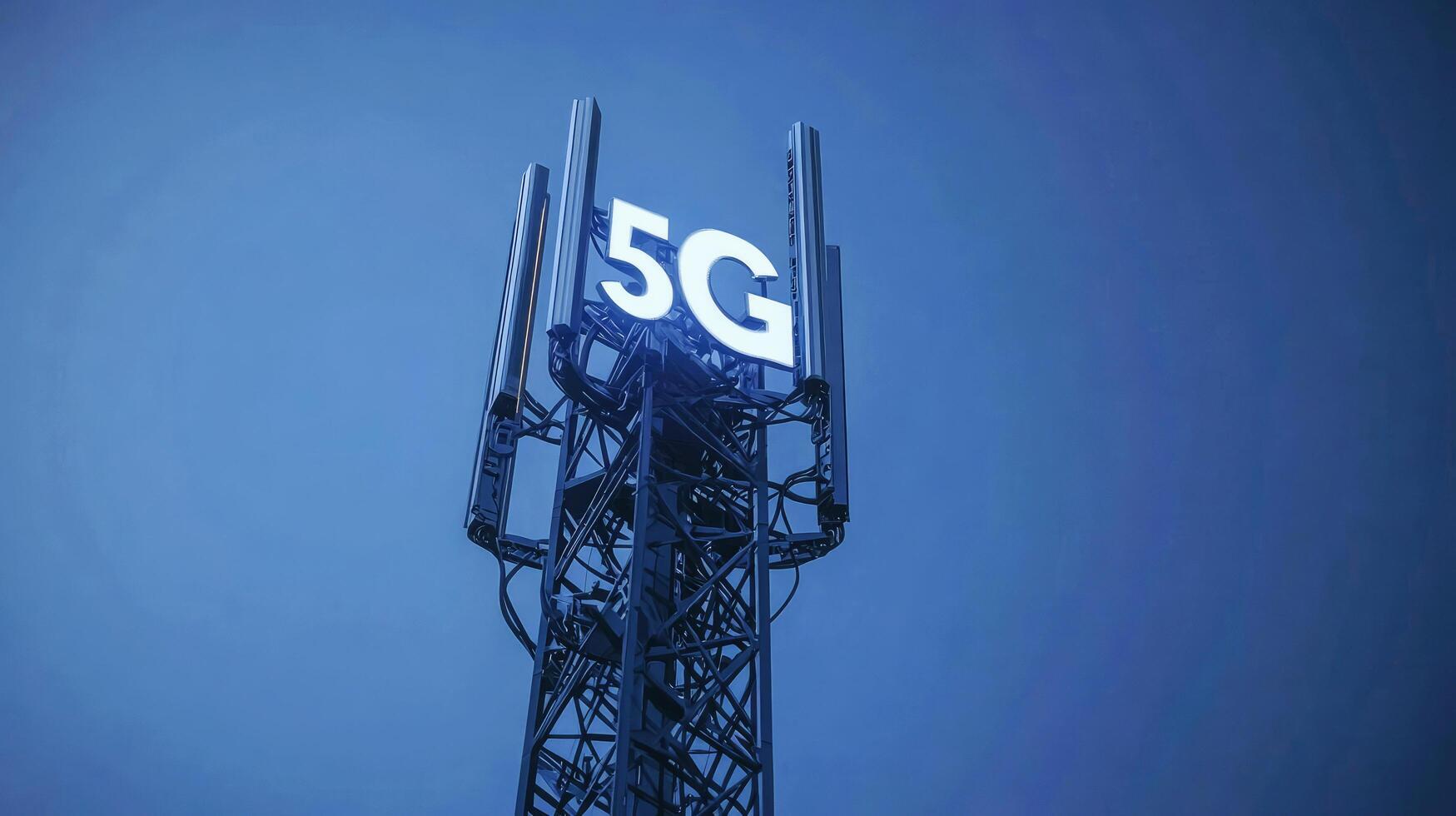 5G cell tower illuminated against a clear blue sky during evening hours photo