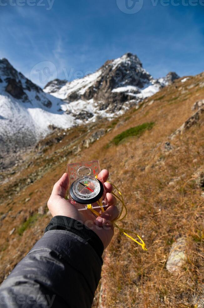 Travel concept. Modern compass against blue sky and snowy mountains in male hand during travel photo
