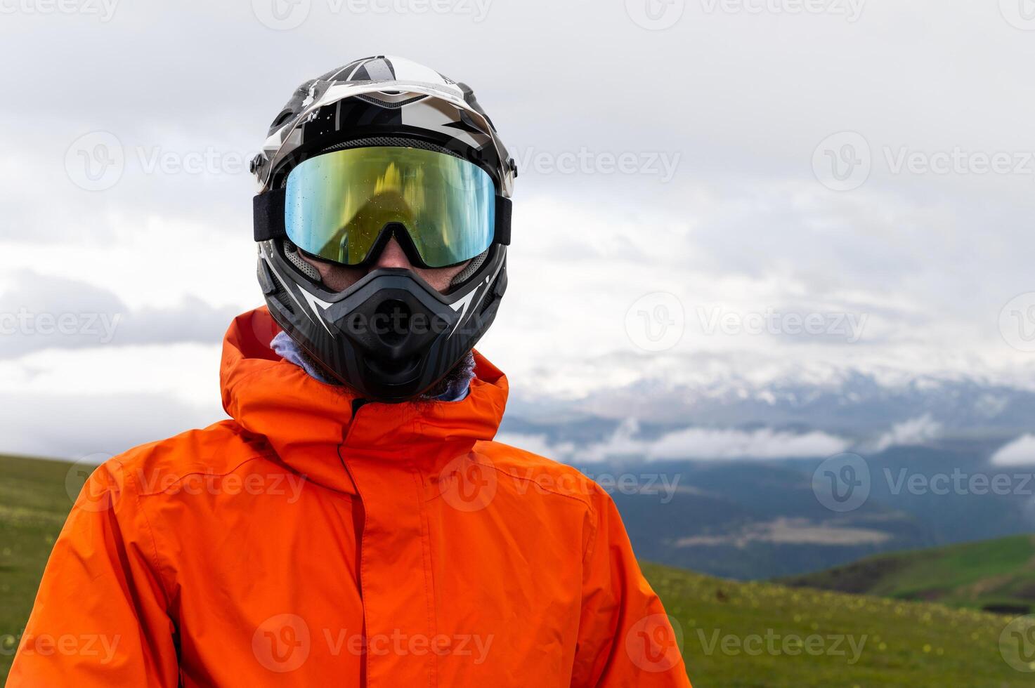 Modern motorcycle helmet with goggles on young guy standing in field with foggy mountains in background, portrait photo