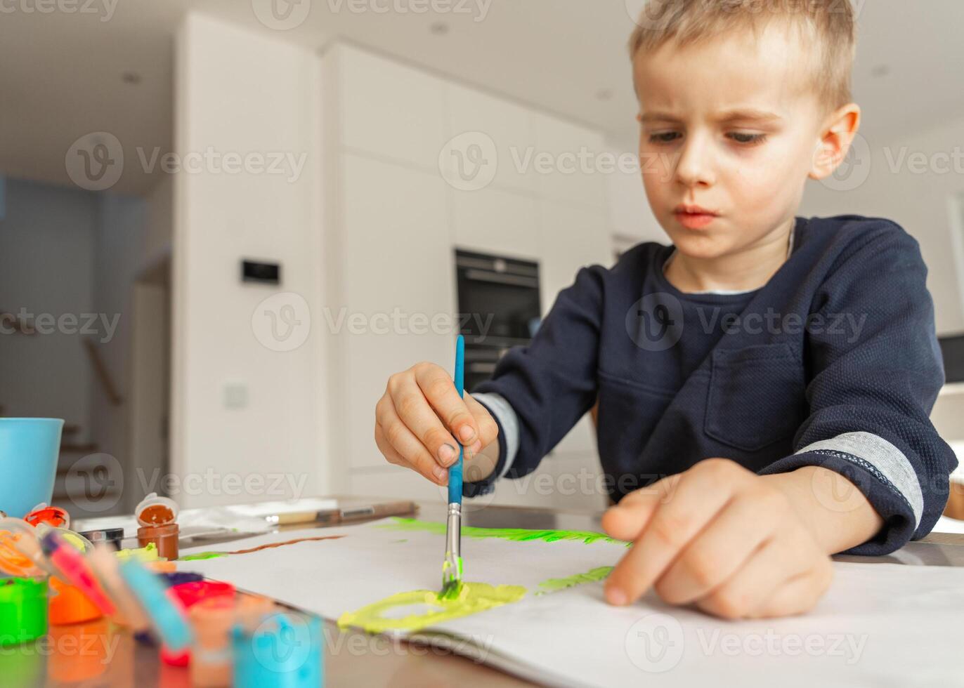 boy draws with acrylic paint on a sheet of paper, a boy of European appearance 4-5 years old draws with paints at home photo