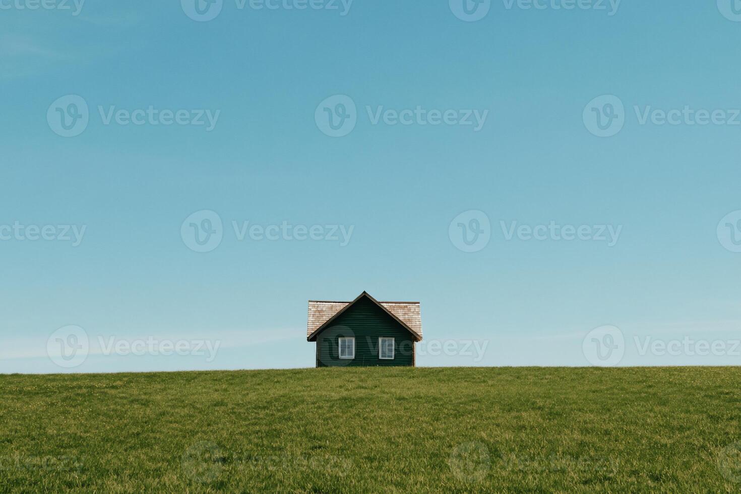 Small, green house on a grassy hill against a clear blue sky photo