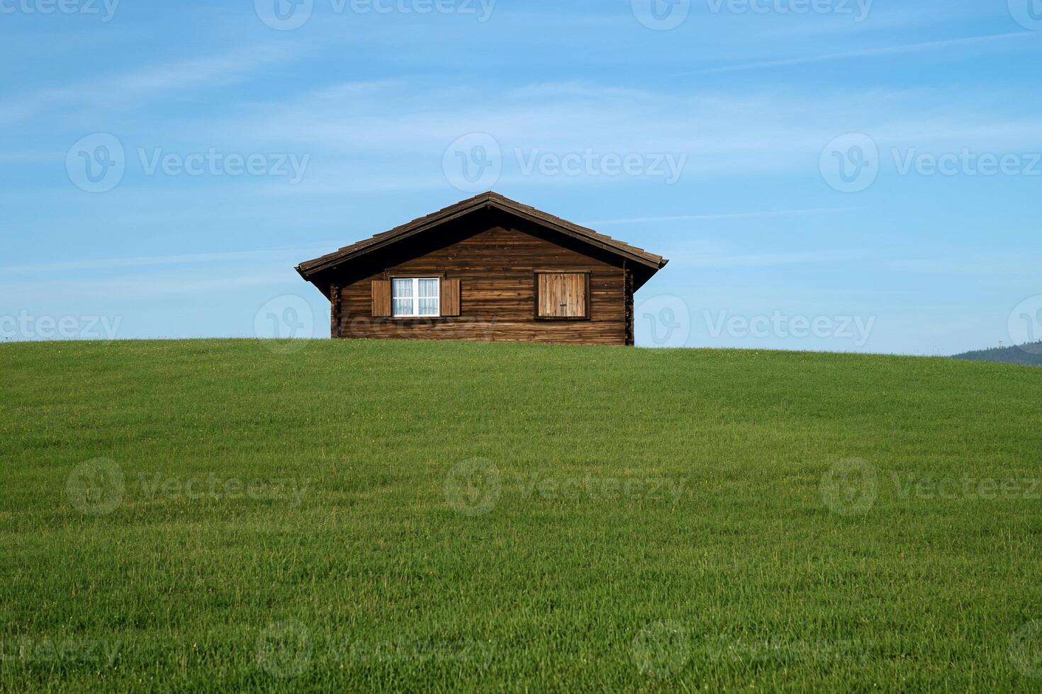 Rustic wooden chalet on a grassy hill under a clear sky photo