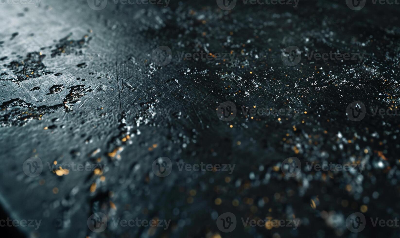 Dark, textured surface with metallic flecks. Detailed close-up view of a dark material with a rough, uneven surface and scattered golden particles photo