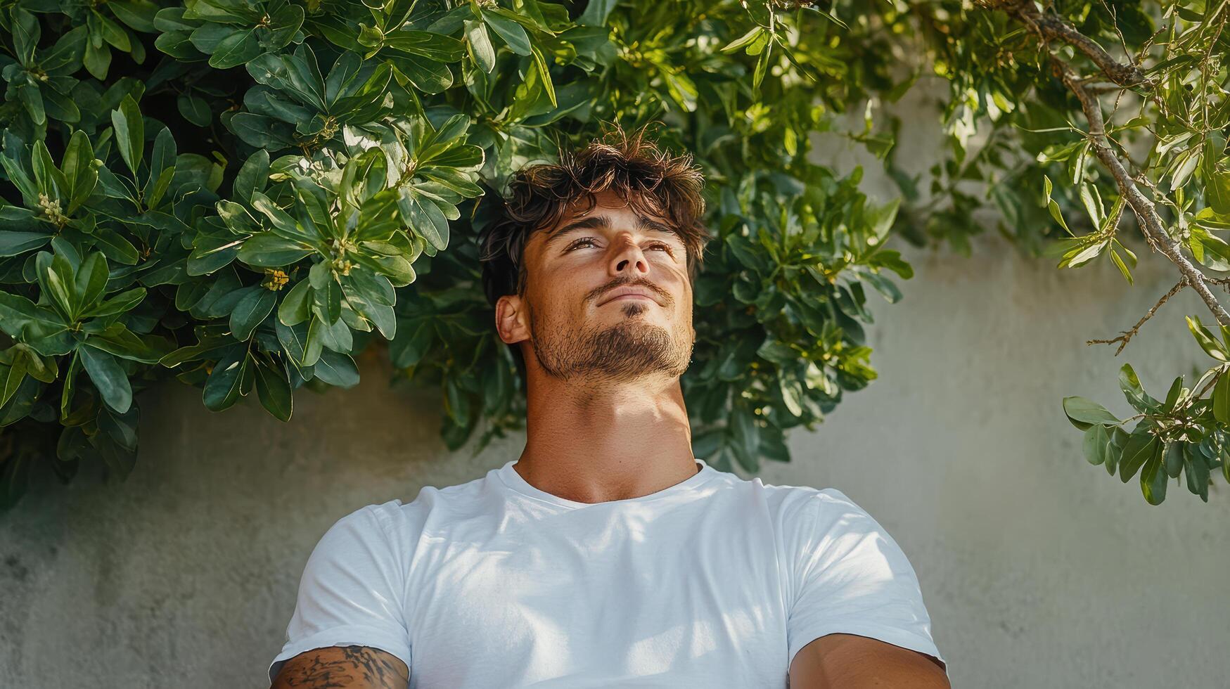 A man in a white t - shirt is leaning against a wall photo