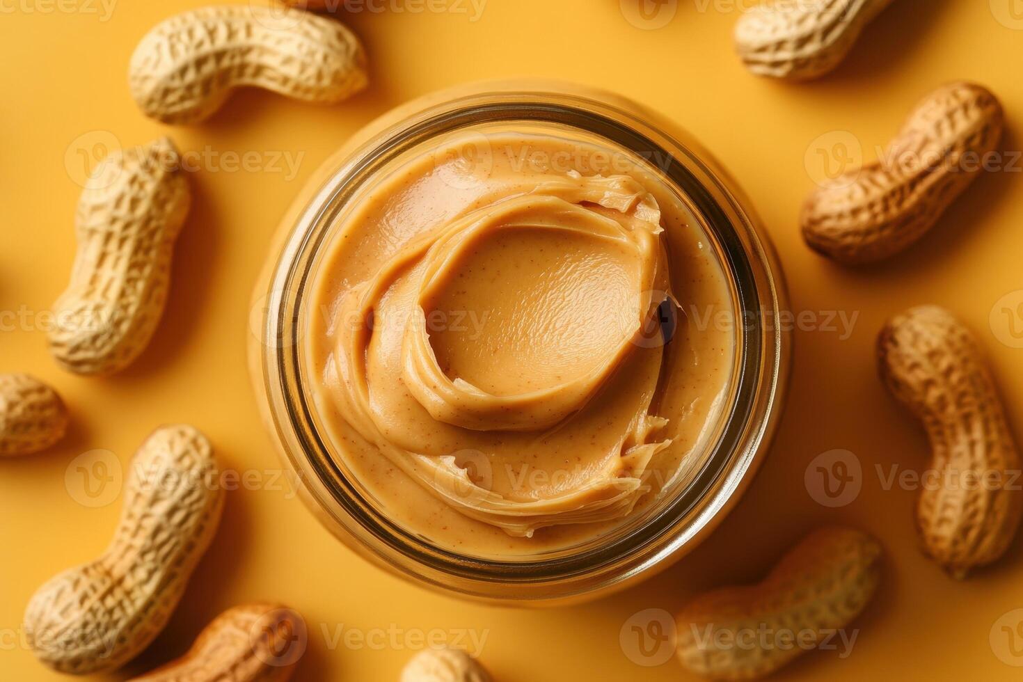 Peanut butter in jar surrounded by whole peanuts on yellow surface photo