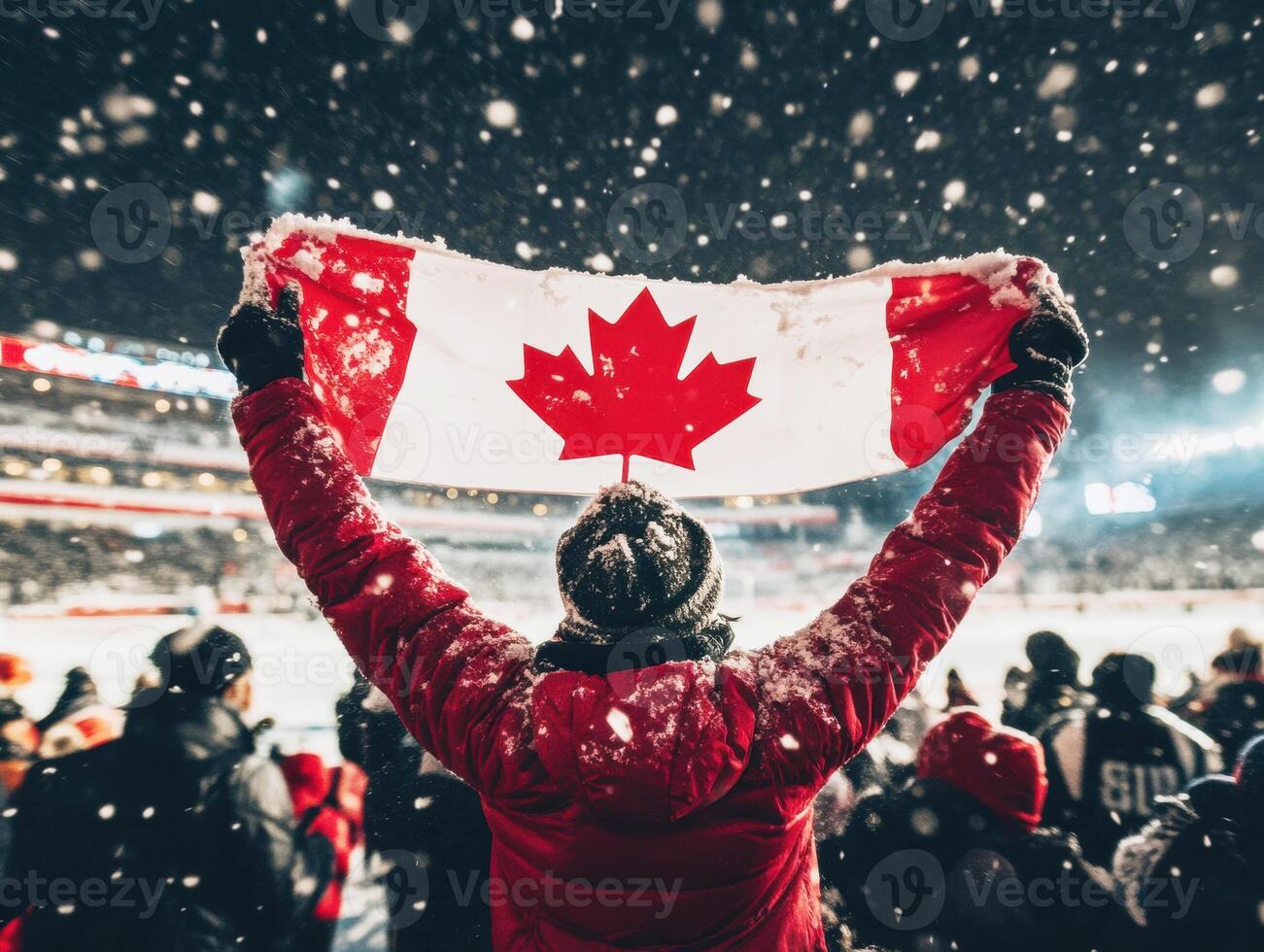 During a snowy outdoor game, a fan in a red jacket proudly holds a Canadian flag high. Passionate supporters surround, creating an energetic atmosphere at the event photo