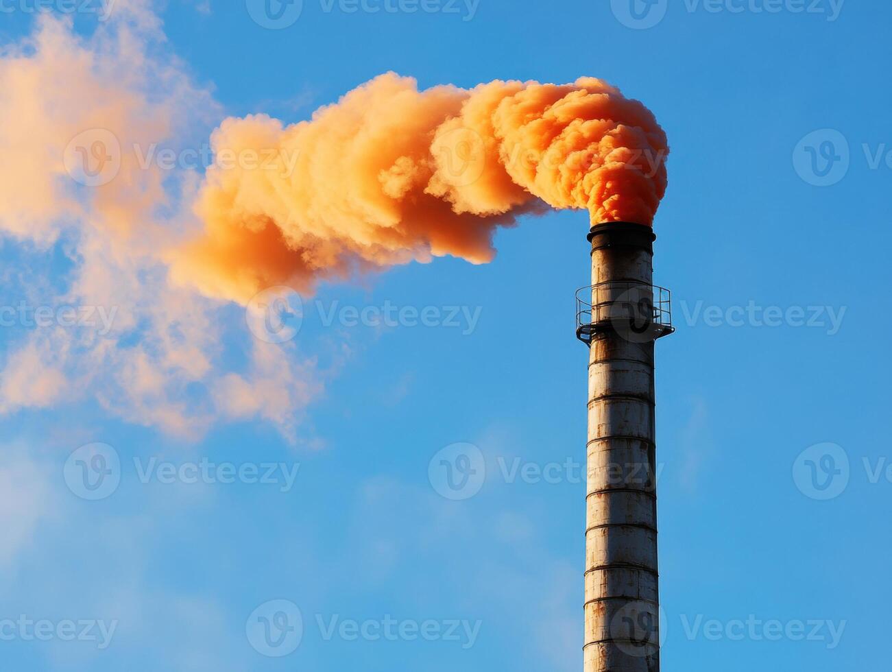 Industrial smokestack emits orange smoke under blue sky photo