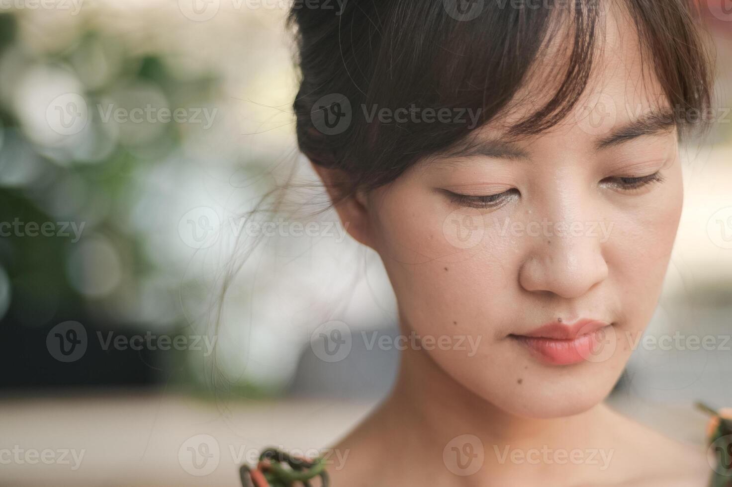 close up of thoughtful Asian young woman with natural makeup, soft lighting, and blurred background, creating serene and introspective mood photo