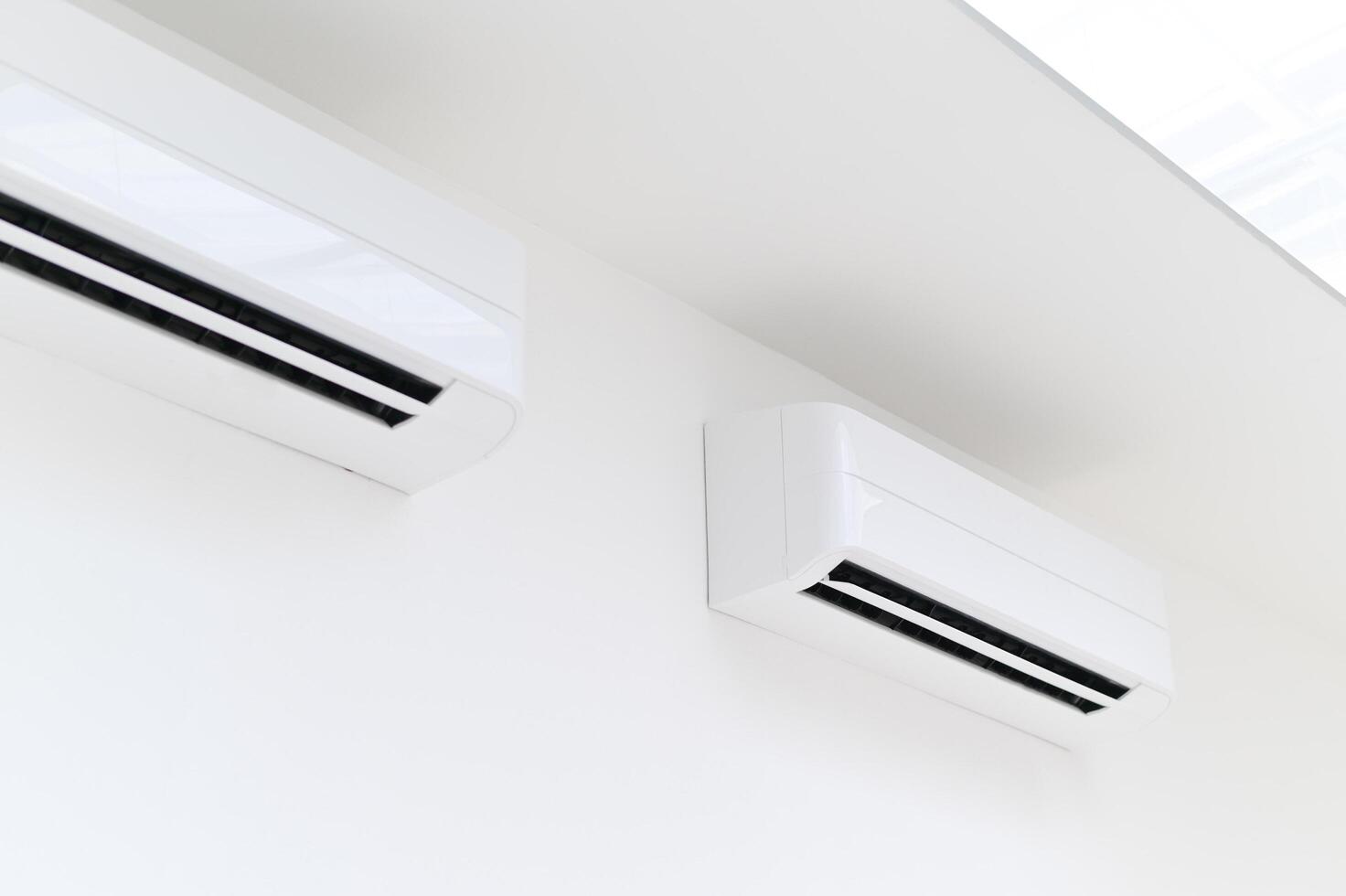 Two air conditioners mounted on the wall in a white room photo
