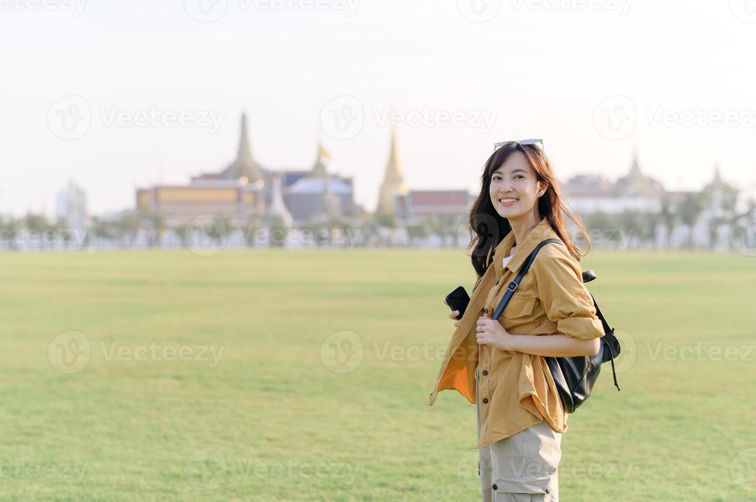 Golden stupas pierce the sky as a young Asian woman in her 30s admires the beauty of Wat Phra Kaew. Discover the splendor of Thai architecture with her. photo