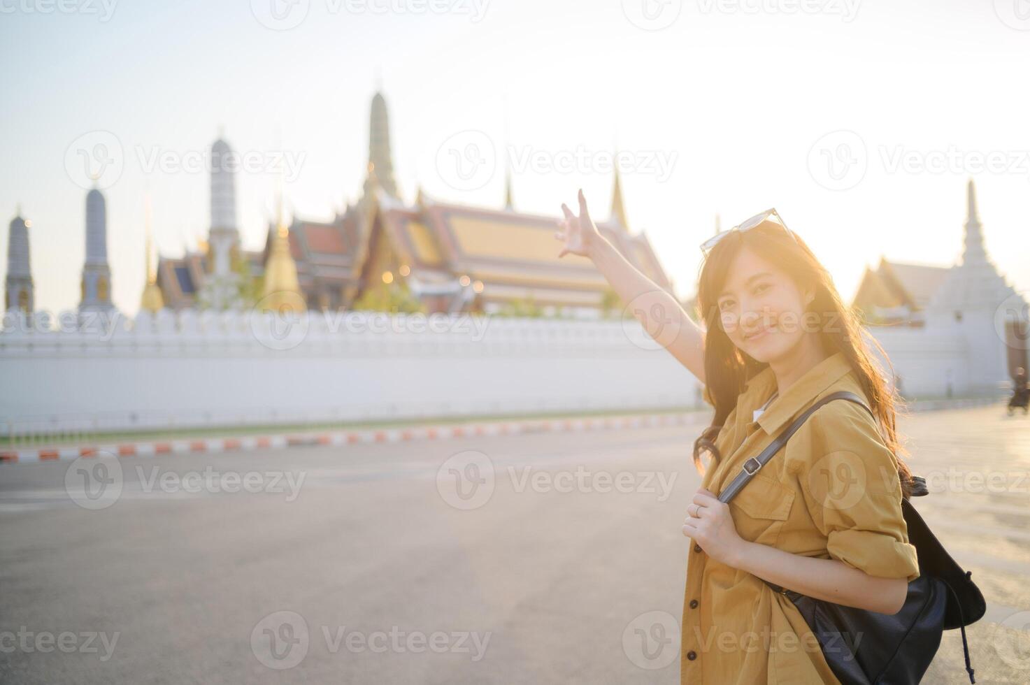 Asian woman tourist in bangkok, thailand, waving her hand in front of the grand photo