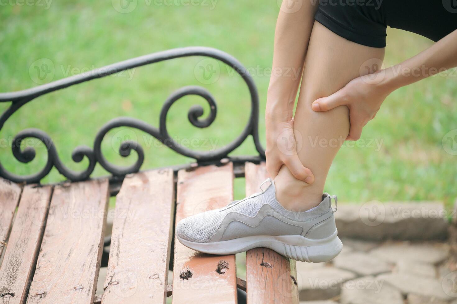 A woman is holding her leg while sitting on a bench photo