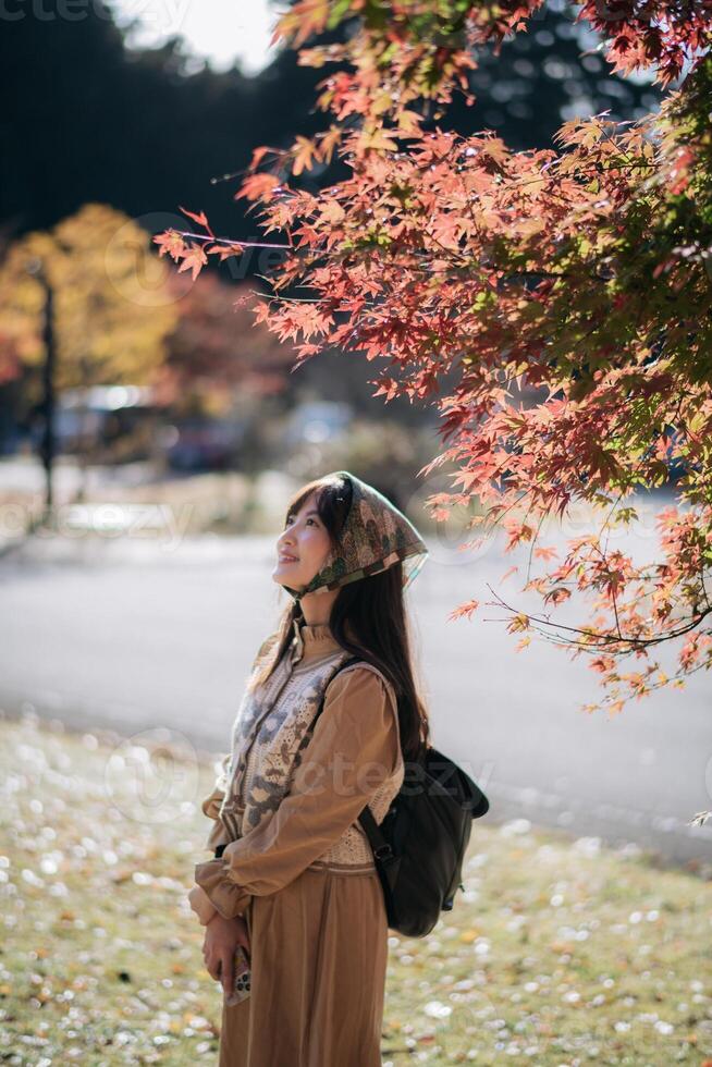 Asian woman in Kyoto fall, wearing a casual dress, enjoys nature's beauty, capturing cheerful smiles amid vibrant foliage and the scenic charm of Japan. photo
