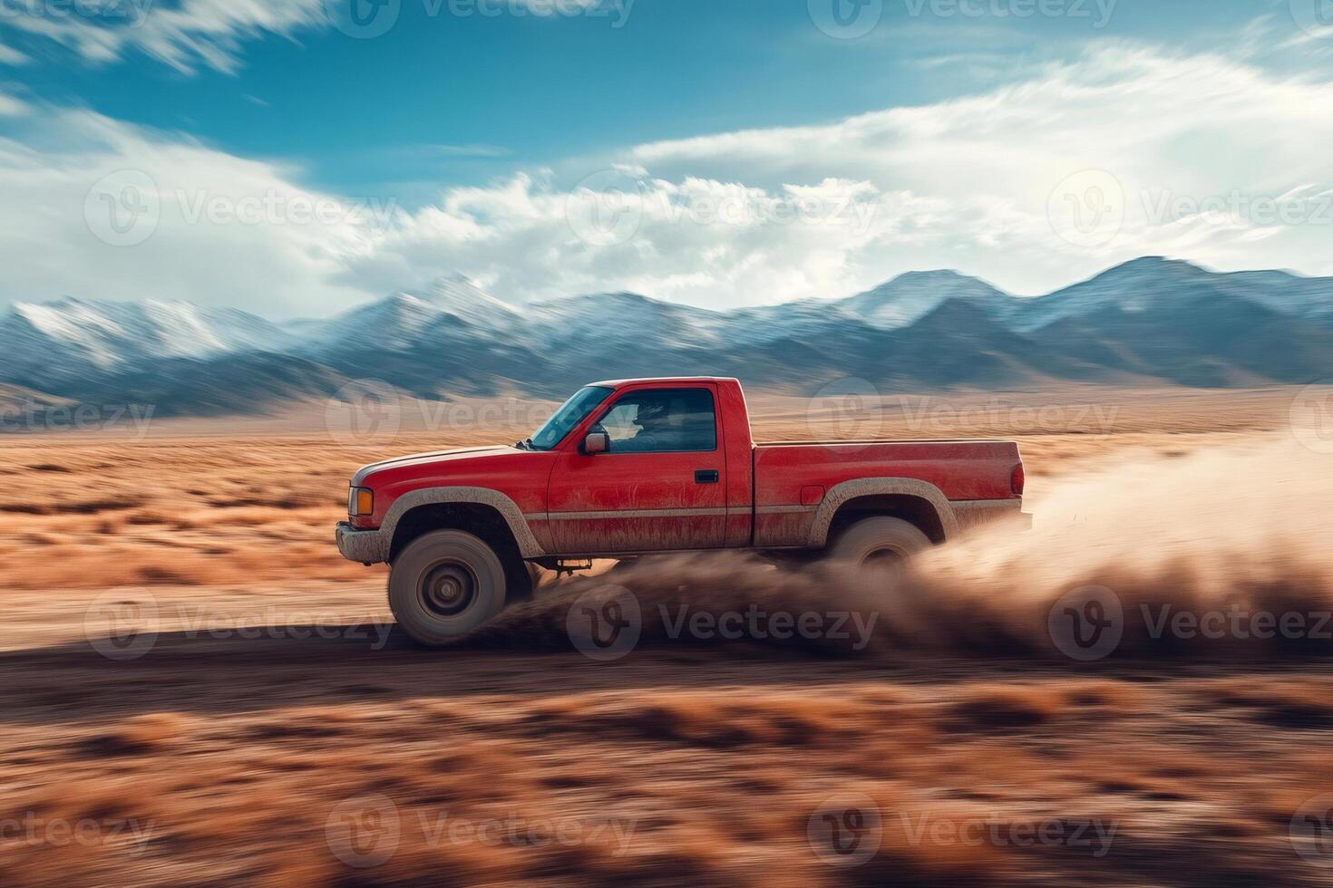 Red pickup truck driving fast on a desert road leaving dust trail with mountains in background photo