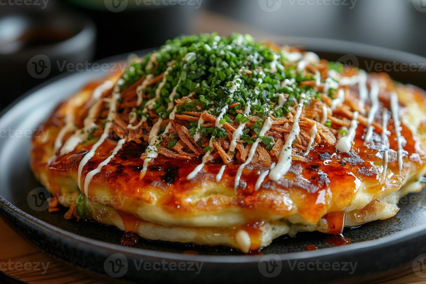 Delicious okonomiyaki topped with crispy fried onions, mayonnaise, and chopped chives, resting on a black plate photo