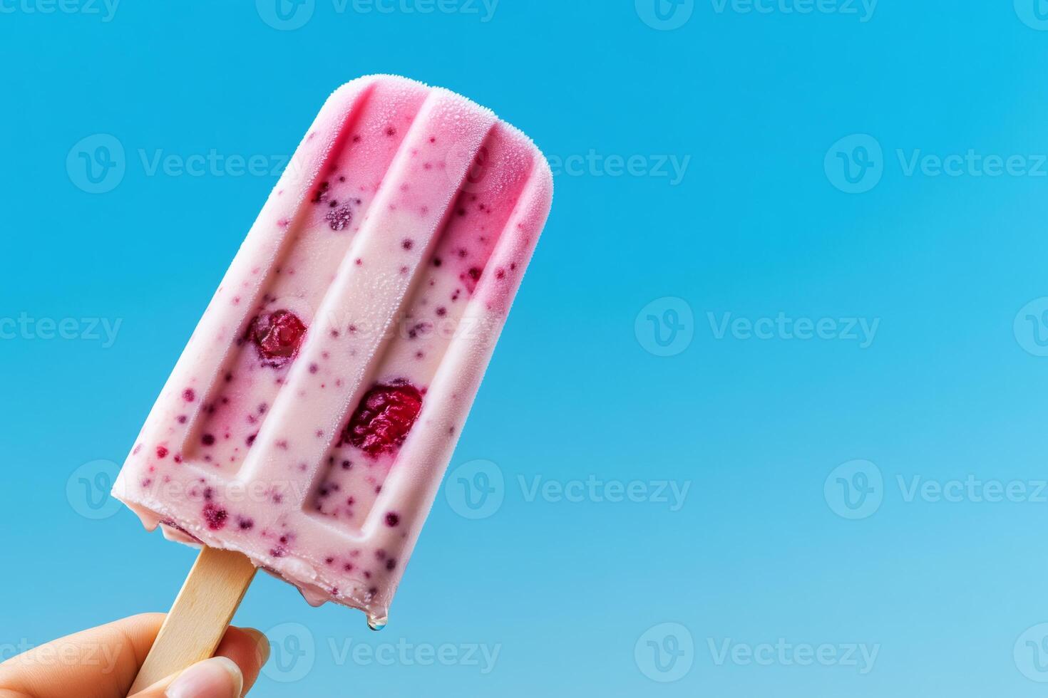 Hand holding melting raspberry ice cream bar on blue background photo