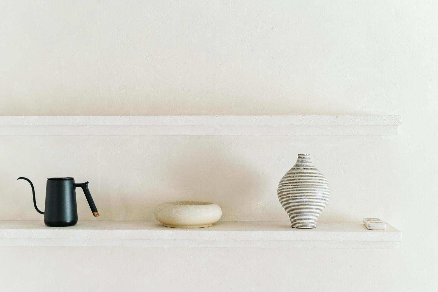Minimalist decor with black kettle, beige bowl, and striped vase on shelf photo
