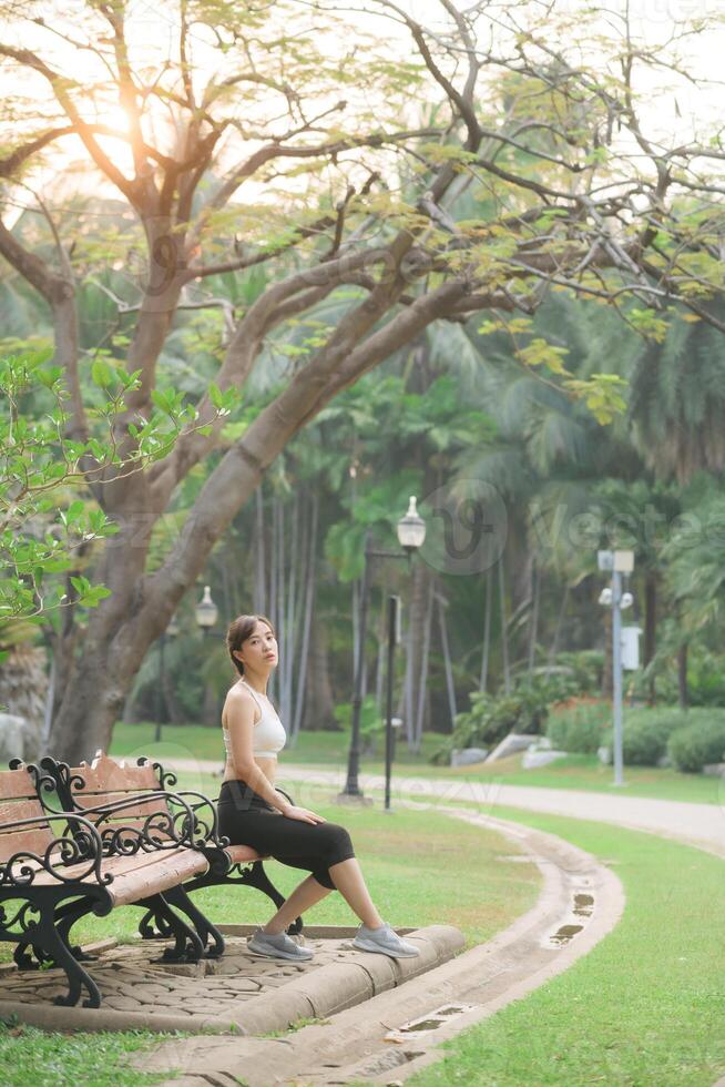 Woman jogger refreshing and sitting over bench in a park after running photo