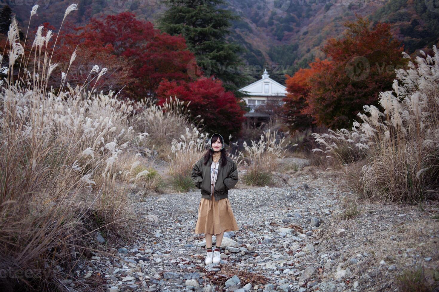 Asian woman in Japan, surrounded by vibrant fall foliage, enjoys a holiday by the lake near Mount Fuji. Friends, selfies, and cheerful moments captured in a joyful portrait photo