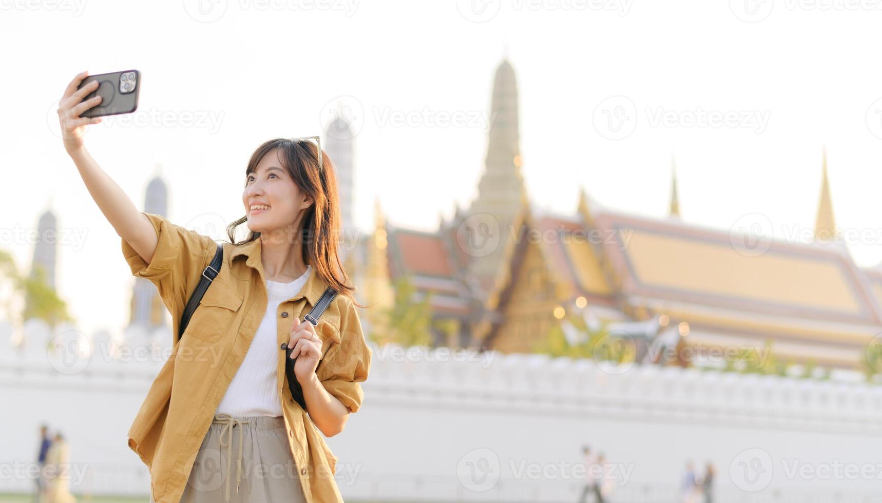 Asian woman taking selfie with smartphone in front of the grand palace photo
