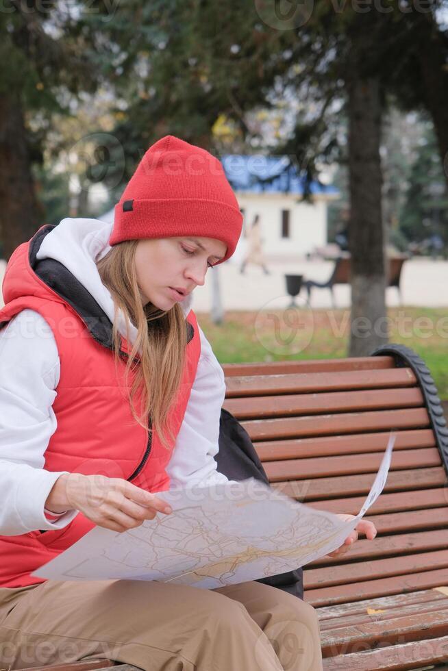 tourist holding map exploring new city and using phone sitting in the park photo