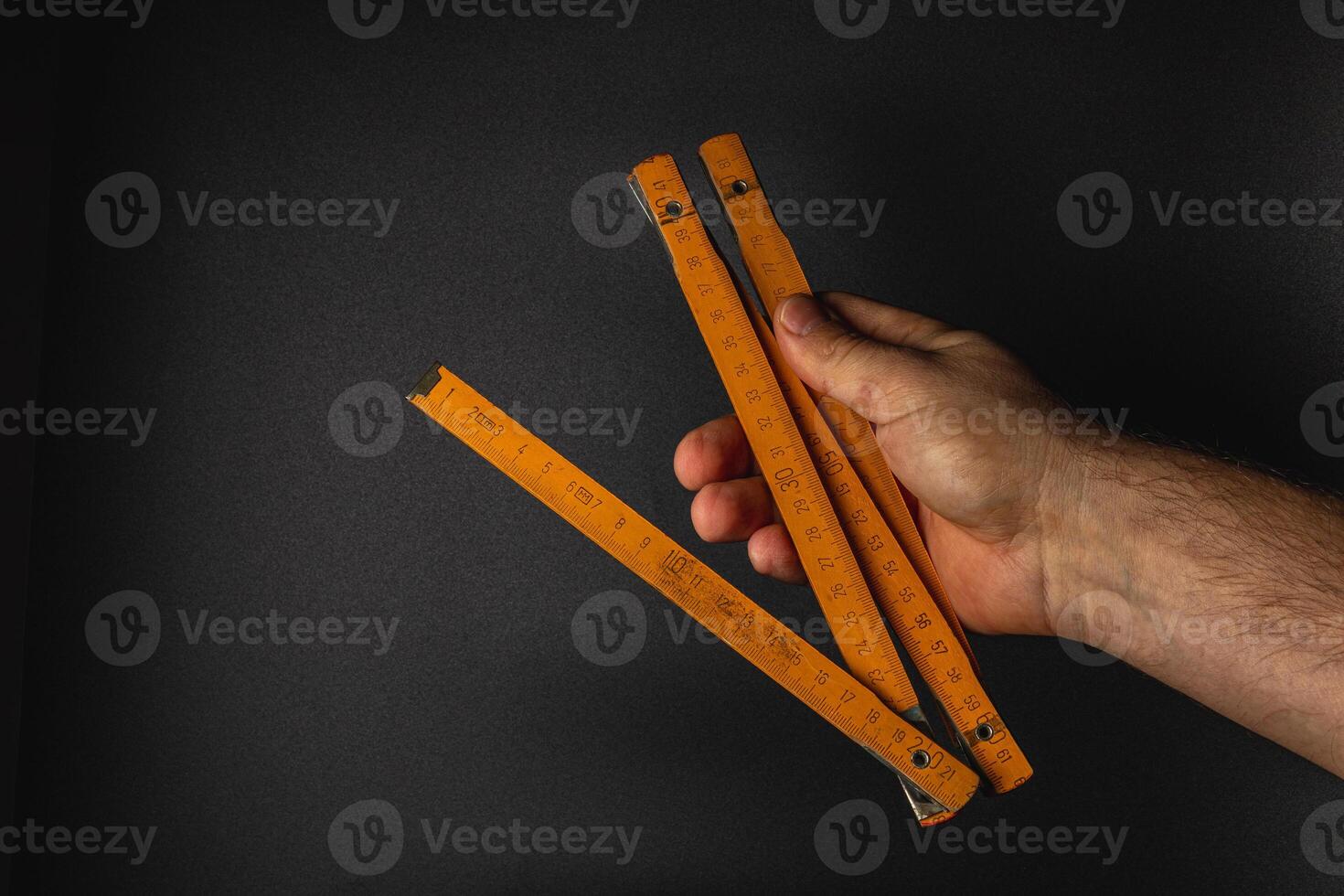 Hand holding wooden measuring sticks against dark background photo