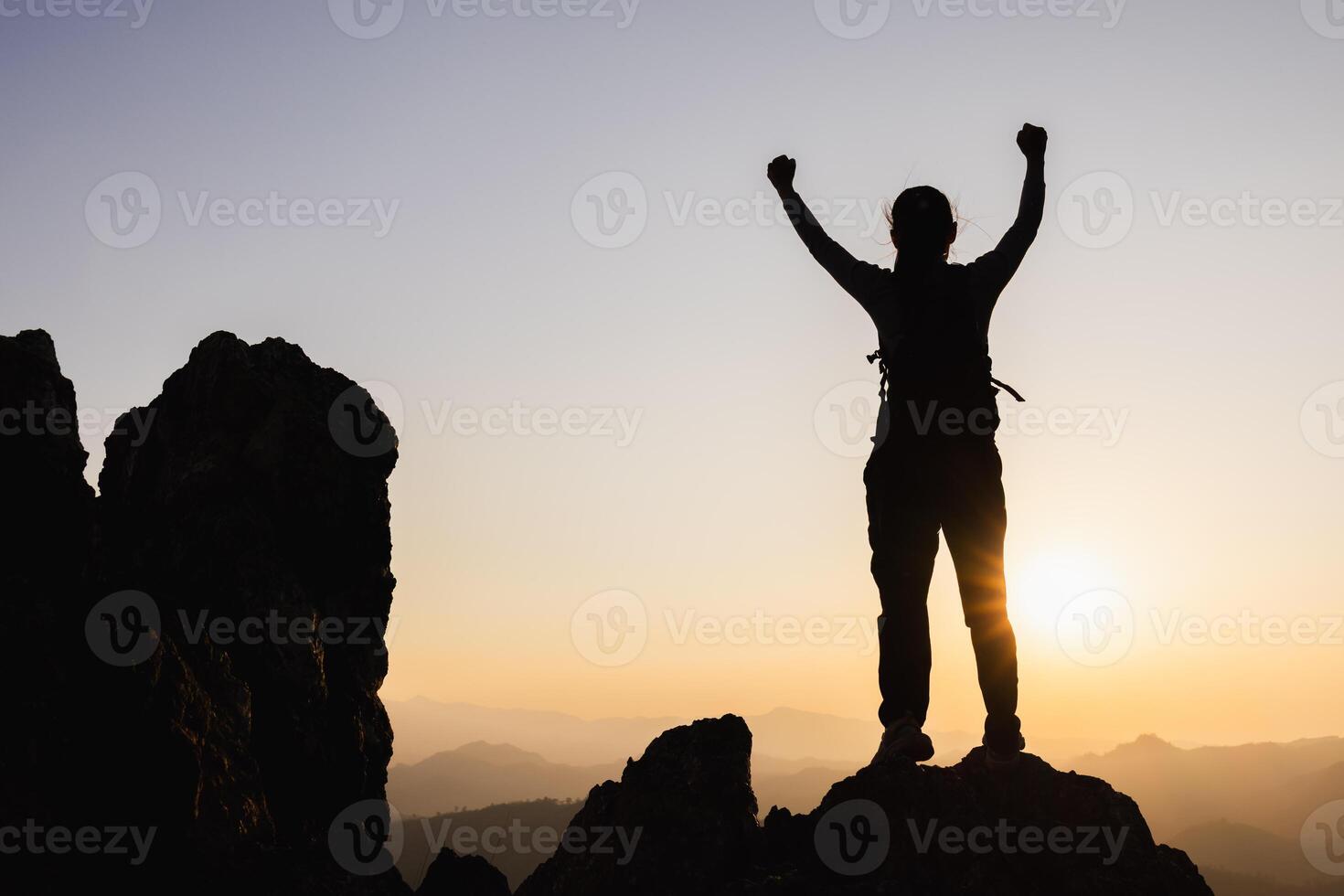 Silhouette of A person standing on top of the mountain with their arms raised in victory, overlooking misty mountains. photo