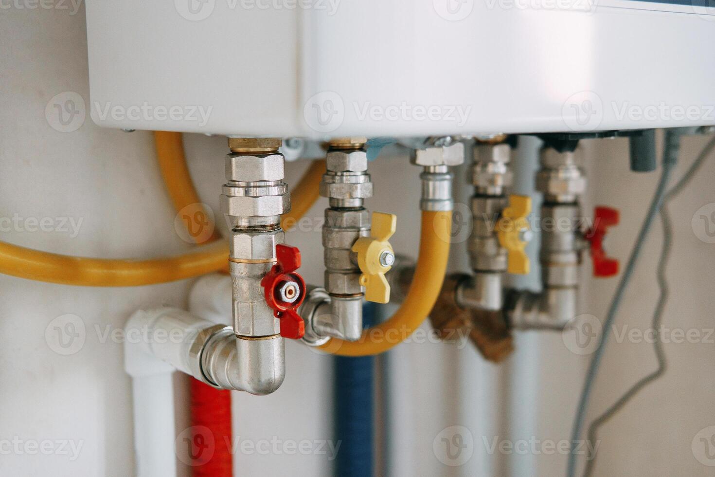 Close-up view of water heater pipes and valves in a utility room, featuring colorful connectors and tubes. Essential components for heating system maintenance and operation. Gas boiler taps photo
