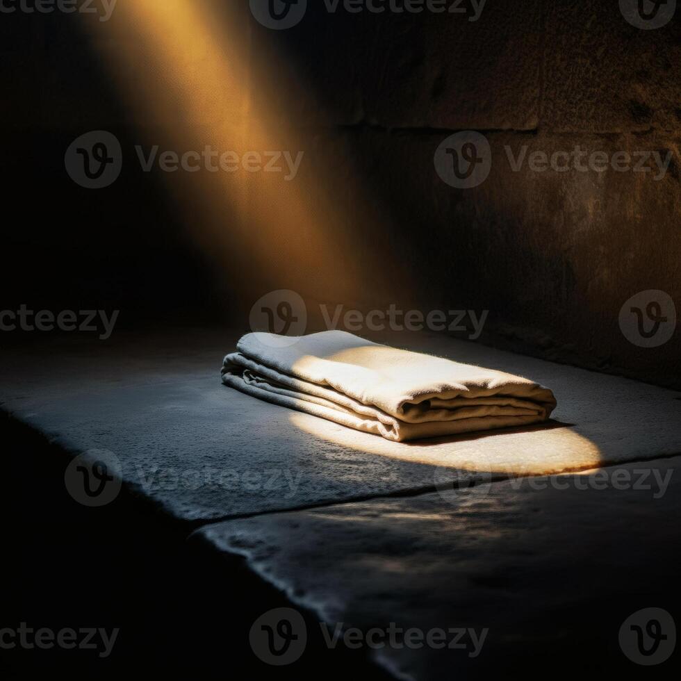 Folded linen cloth illuminated by a golden beam of light in a dark stone room, evoking themes of resurrection and mystery photo
