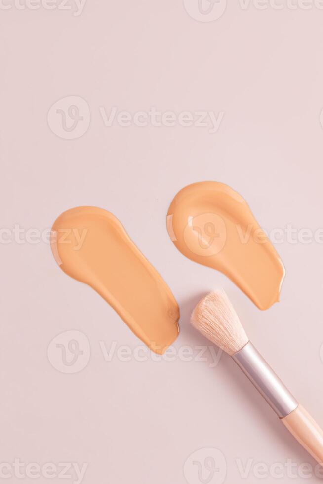 Two cosmetic strokes of natural tone liquid foundation powder on a beige vertical background with a makeup brush. top view. copy space. texture sample photo