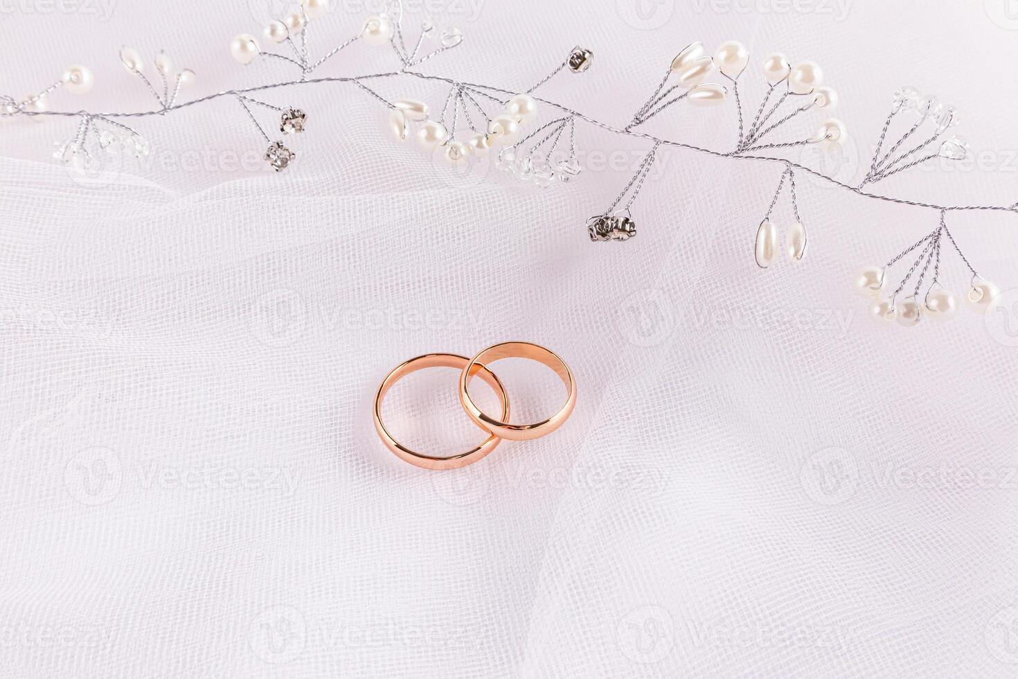 A beautiful wedding arrangement with two gold wedding rings and a pearl and rhinestone hairstyle decoration. white tulle background. photo