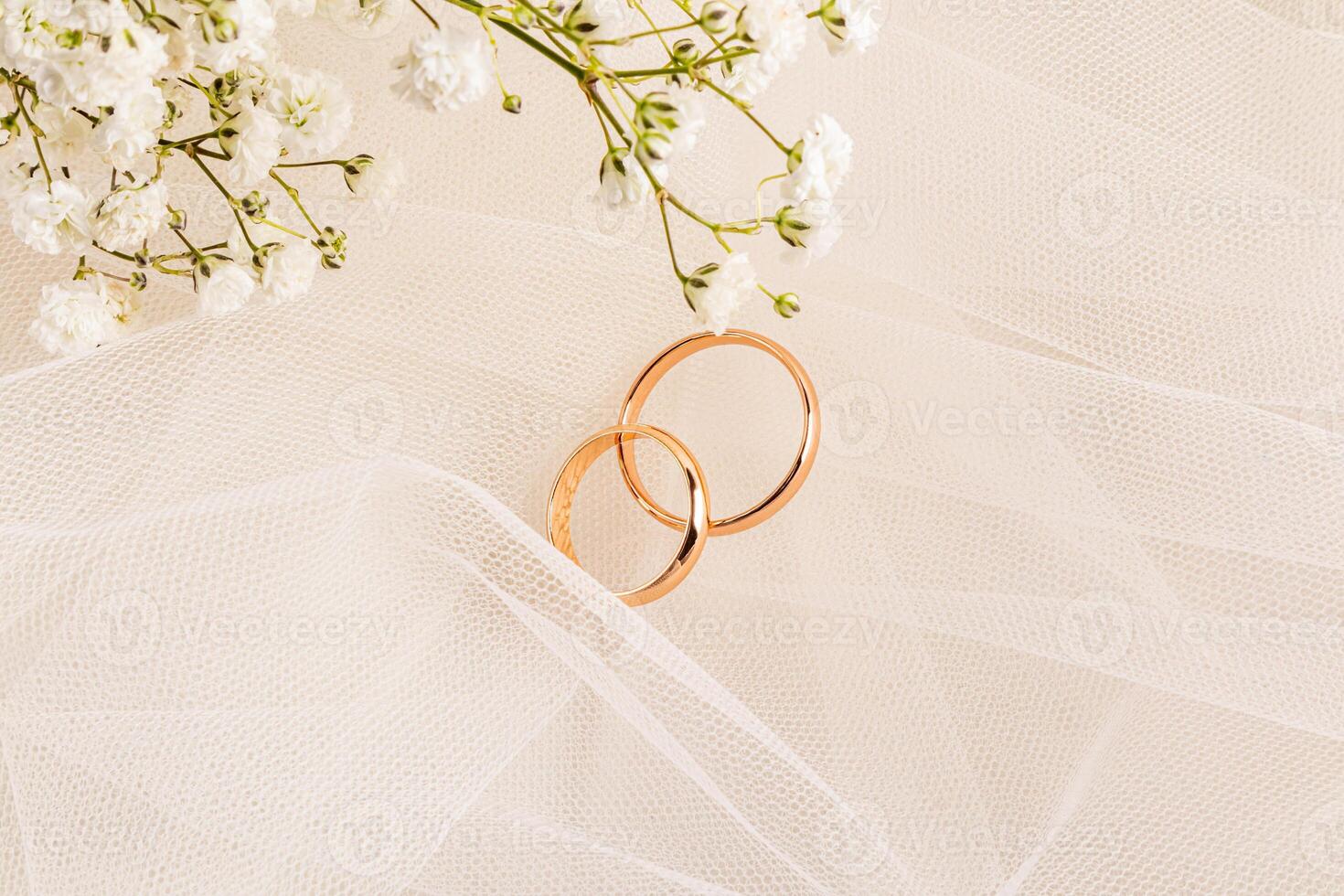 Two gold classic wedding rings among the delicate folds of bride's beige veil and delicate gypsophila flowers. wedding concept. layout. invitation. photo