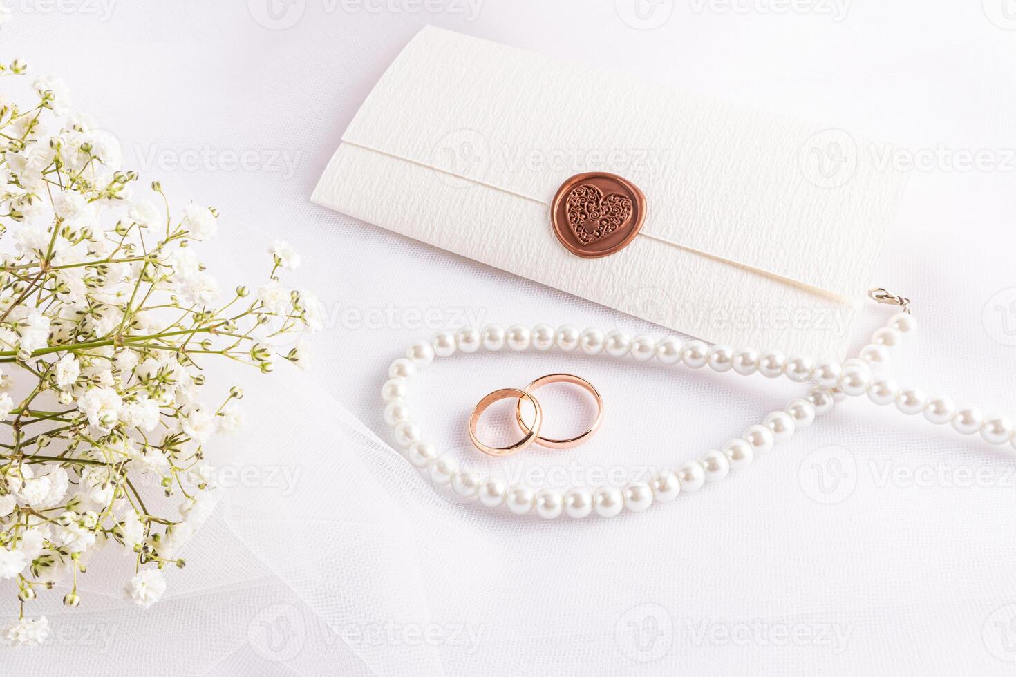 A layout, a sample of a wedding card or invitation in a classic white tone with gypsophila flowers, pearl beads, rings, an envelope. photo
