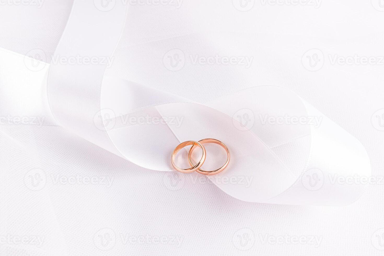 Chic wedding background for wallpaper design, postcard, invitation. Two elegant wedding gold rings lie on white satin wide ribbon beautifully folded. photo